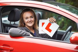 Woman in a red car holding L plates and smiling