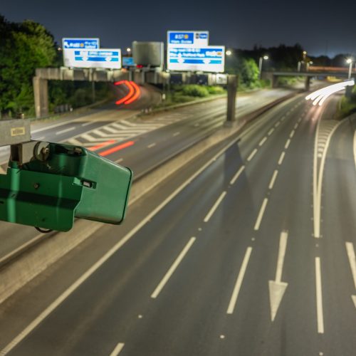 ANPR vehicle surveillance. An ANPR camera on the motorway monitoring traffic flows and speed at night. Light trails of passsing vehicles can be seen,.